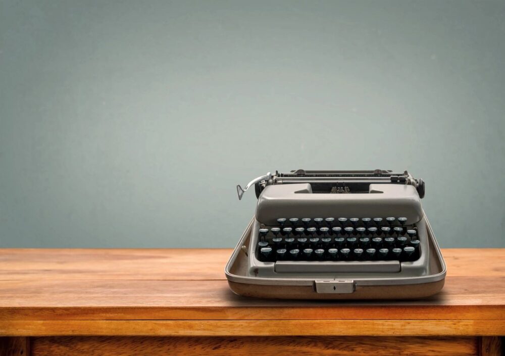 a typewriter on a wooden table with a gray wall in the back